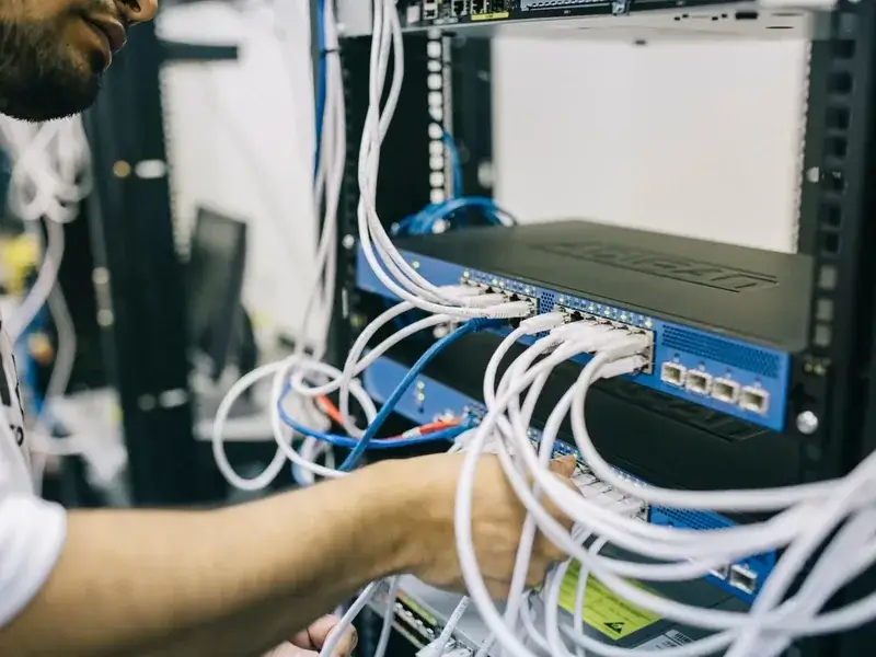 Engineer connecting network cables to a switch in an equipment rack during an E1 PRI gateway installation