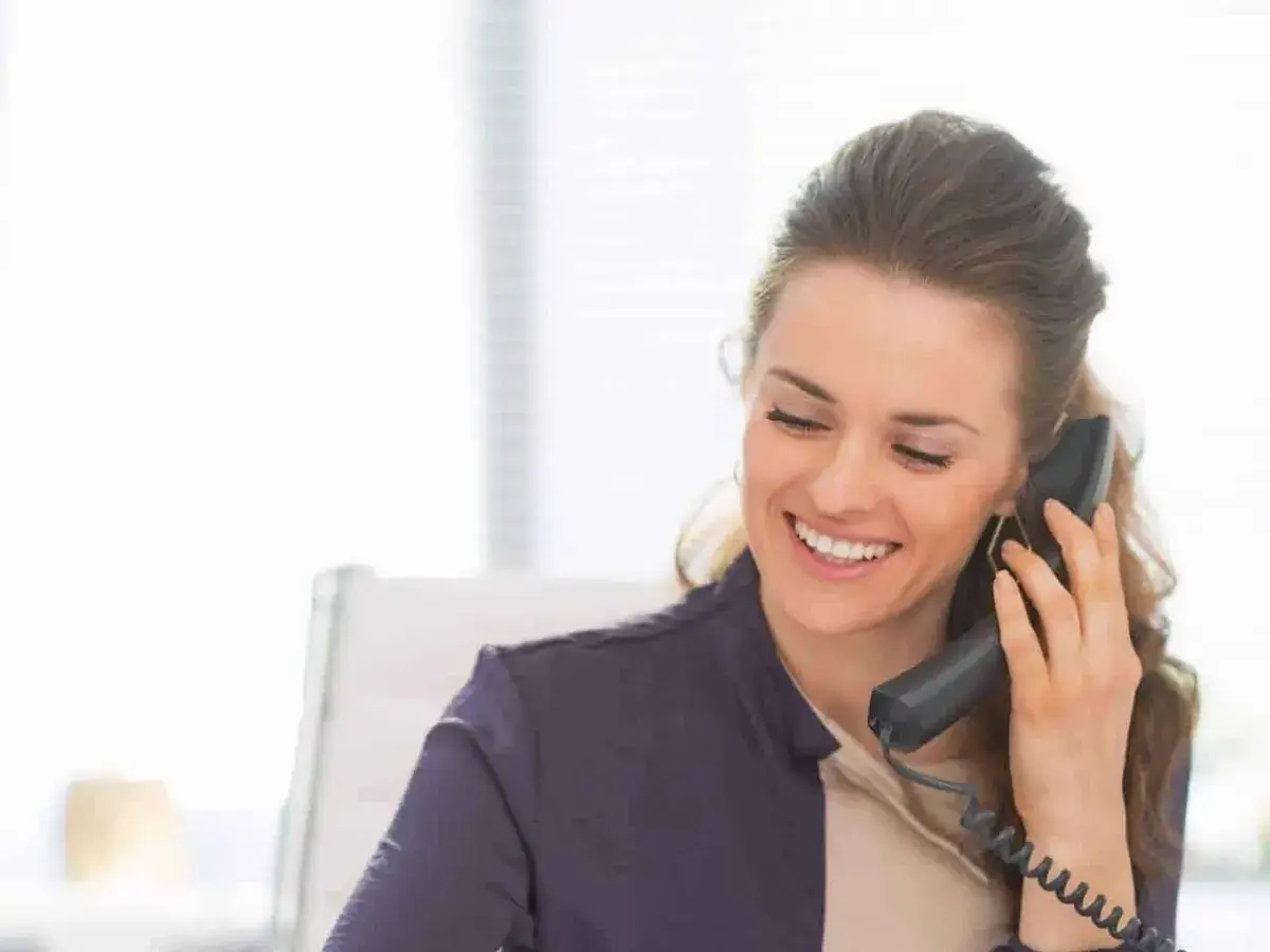 Businesswoman smiling while taking a call on a desk phone connected to a Sangoma PBXact UC phone system